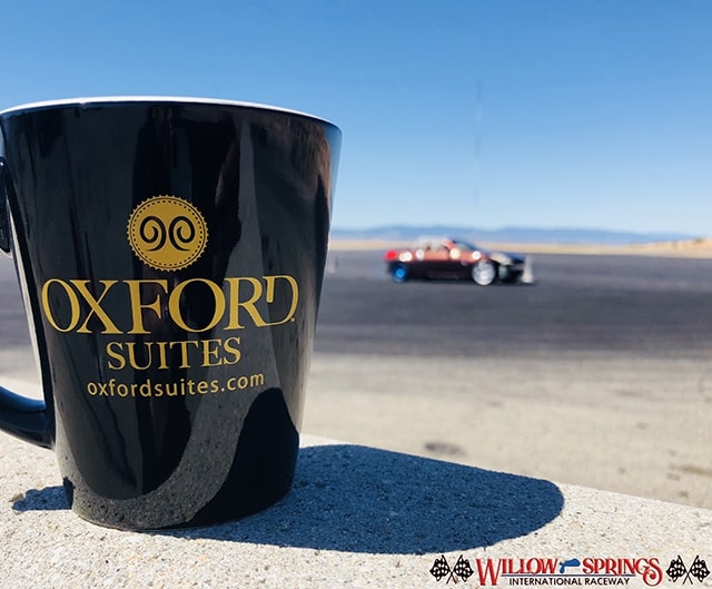 Photo of an Oxford Suites mug with a racetrack in the background.